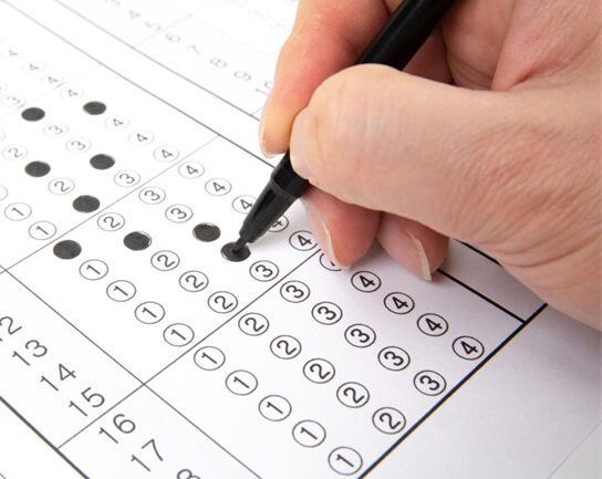 A picture of a hand holding a pen and a 5 point survey which is part-filled in