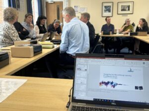Conference attendees in the background and a PC, on a desk, showing a slide in presenter view in the foreground
